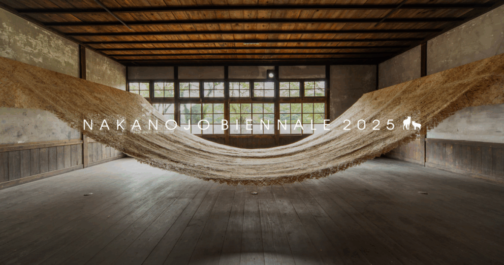 Art installation featuring a large, suspended textile within an artistic space, with large windows allowing natural light.