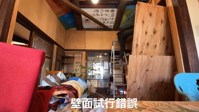 A cozy room filled with fabric and plants, featuring a wooden ladder leading to a rustic loft area with artwork on the ceiling.