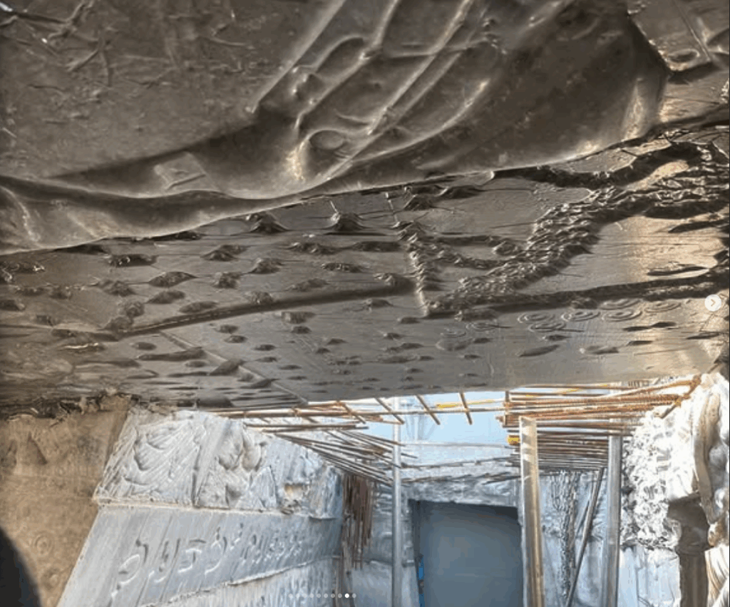 Underside view of intricately carved stone reliefs at a construction site, showcasing textured surfaces and historical motifs.