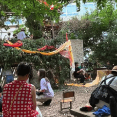 People enjoying an artistic space surrounded by greenery, with colorful decorations and a makeshift stage.