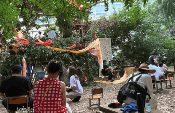People enjoying an artistic space surrounded by greenery, with colorful decorations and a makeshift stage.
