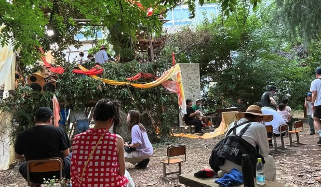People enjoying an artistic space surrounded by greenery, with colorful decorations and a makeshift stage.